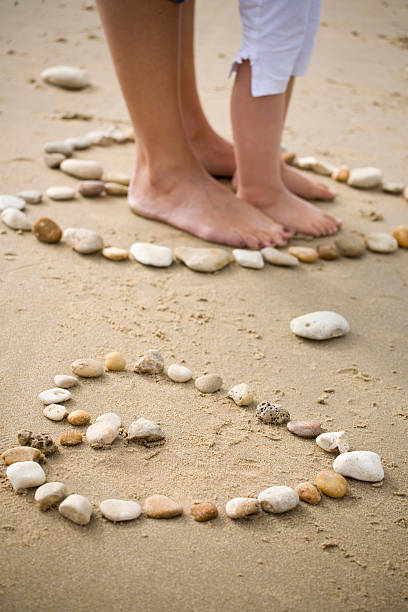 two hearts of pebbles with the feet of a woman and her child in one of them